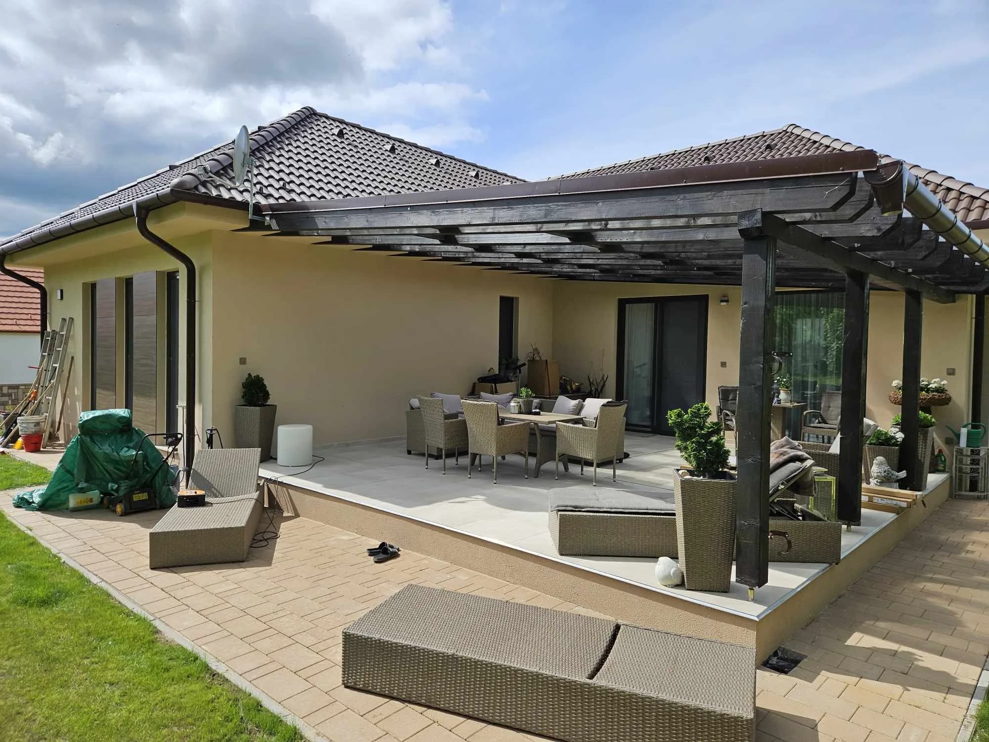 Sötét fa pergola bútorozott teraszon, családi ház mellett